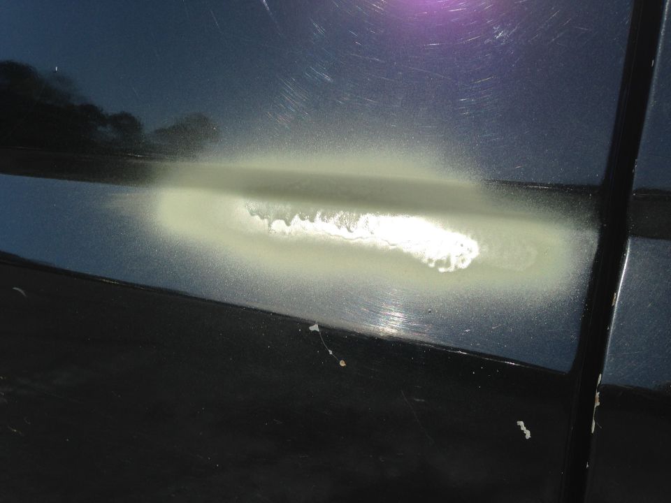 close-up of damage on dark car body, showing primer and paint repair