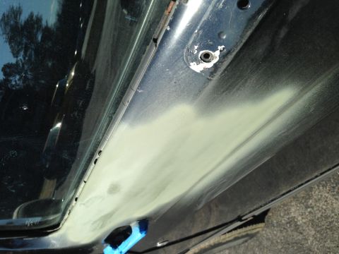 1990 Ford Bronco - Body filler is applied to a section of a car door panel, indicating repair work.