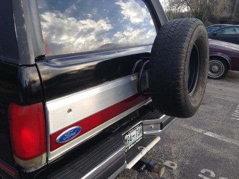 1990 Ford Bronco - Rear view of a black Ford Bronco, a spare tire and a chrome bumper. Another vehicle is visible in the background.