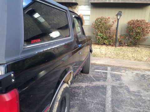1990 Ford Bronco - A black SUV is parked outside a building with bushes and a lamppost nearby.