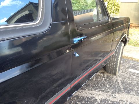 1990 Ford Bronco - Side view of a black Ford Bronco with red trim, showing its body style and a door handle covered in blue tape.