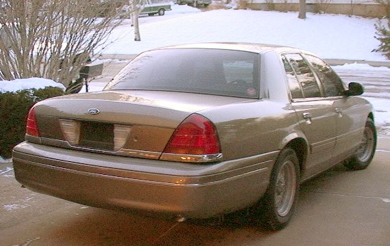 Tan Ford Crown Victoria sedan seen from the rear driver-side quarter on a snowy driveway