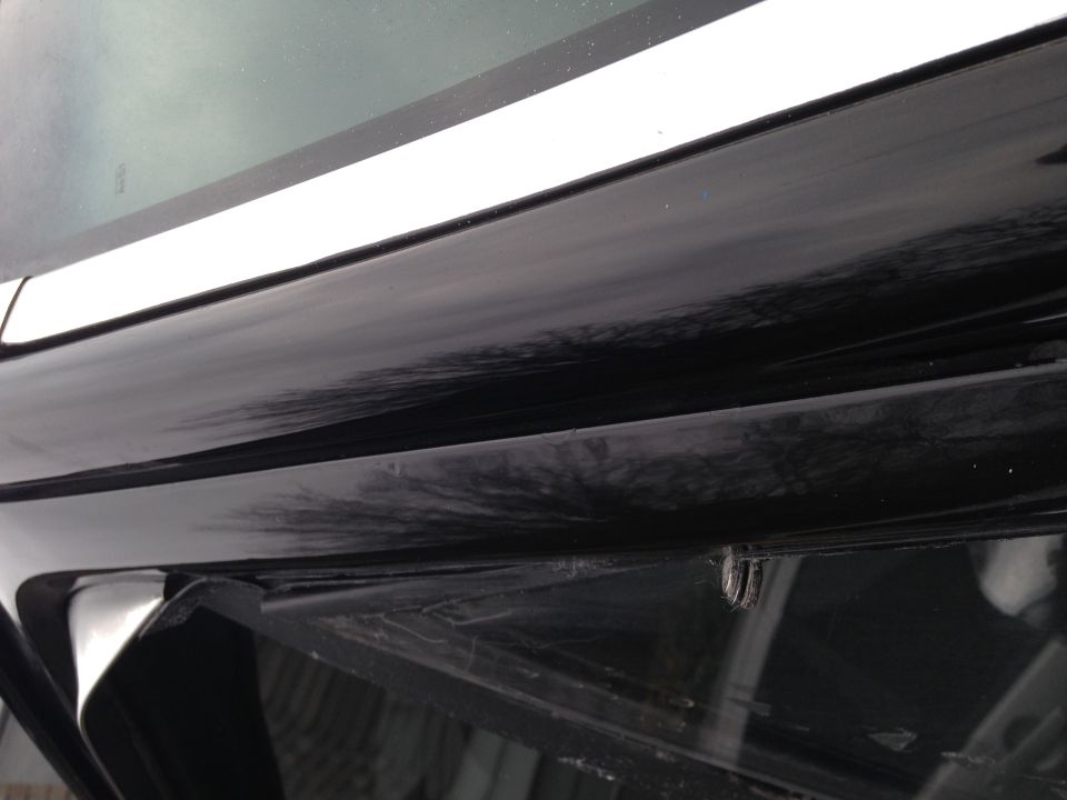 Black car door edge with a white trim piece above it. A small metal clip is visible