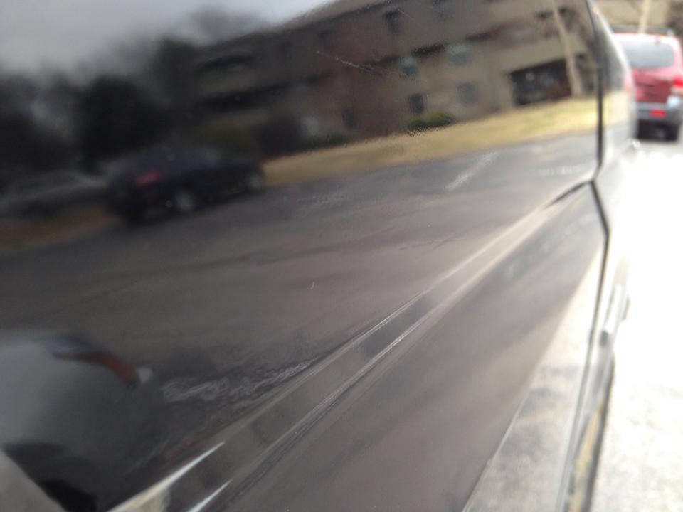 Black vehicle side panel with reflections of buildings and another vehicle