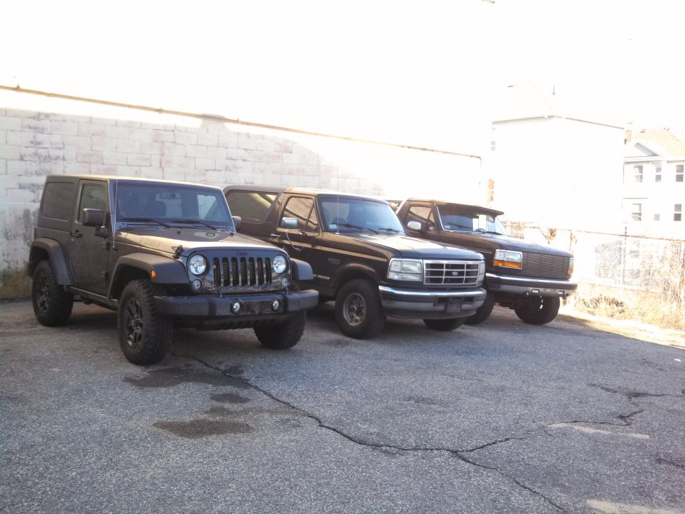 Dark gray Jeep Wrangler parked next to two dark Ford trucks