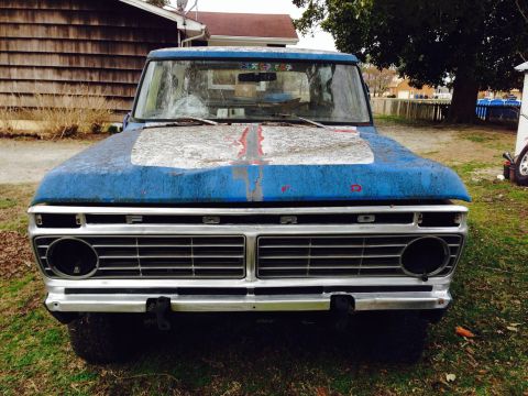 1979 Ford Bronco - This weathered Ford truck sits in a yard, showing its distinctive grille and faded paintwork.