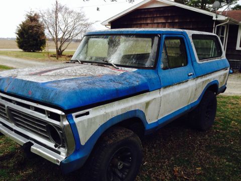 1979 Ford Bronco - This weathered blue and white Ford Bronco sits on a grassy area next to a house.