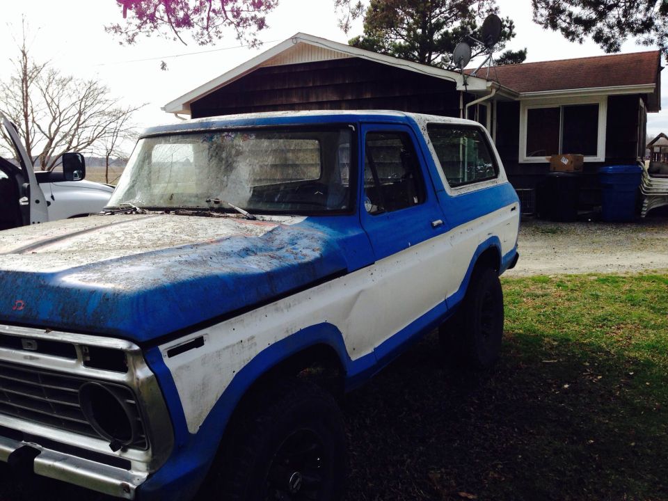 Blue and white Ford Bronco parked in a yard with a house in the background