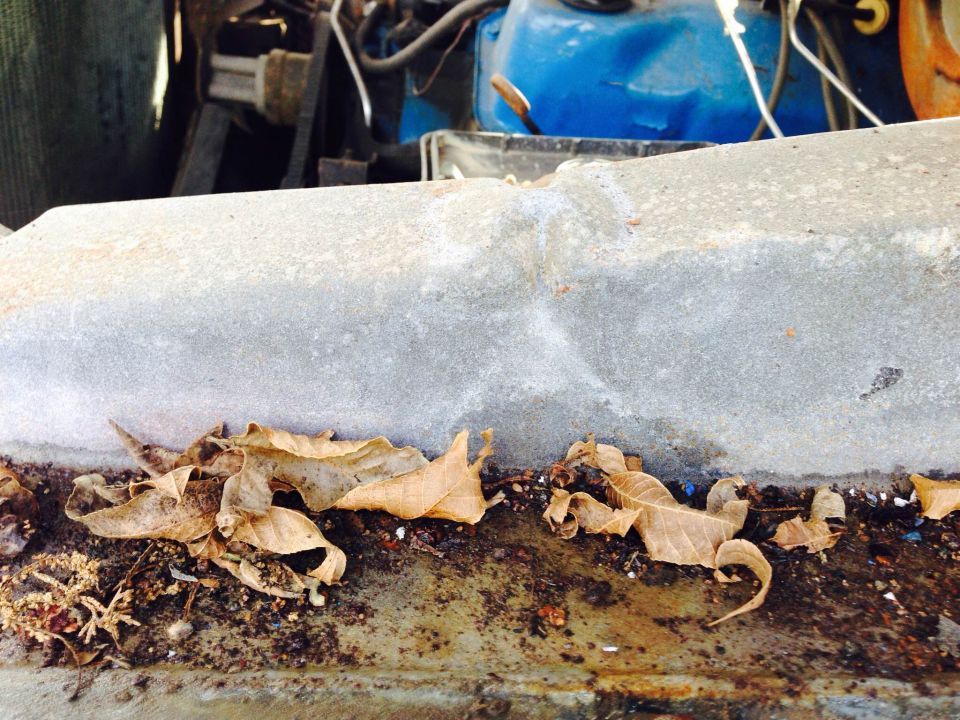 close-up of engine bay with blue fluid reservoir and fallen leaves on a dirty surface