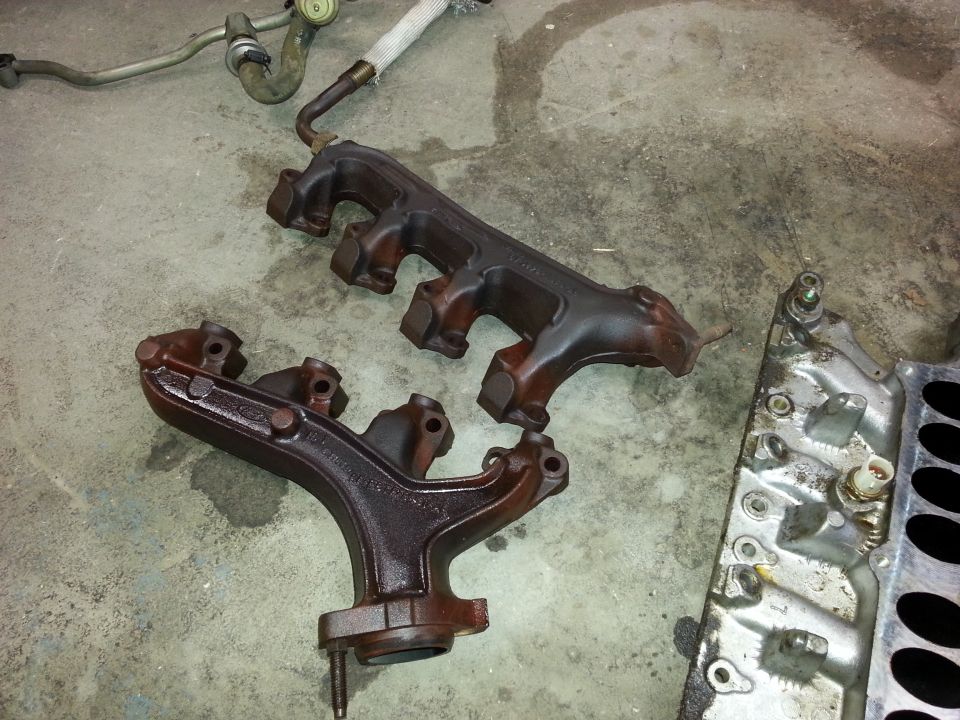 Two cast iron exhaust manifolds and a silver intake manifold on a concrete floor