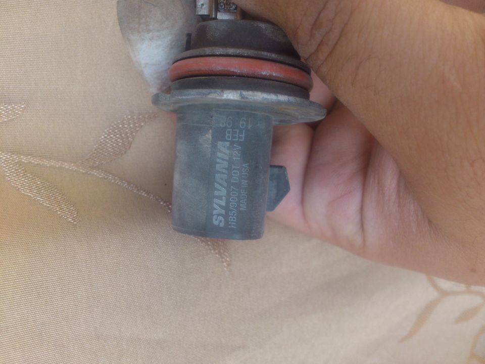 Sylvania HB5/9007 DOT headlight bulb with red seal, held by hand