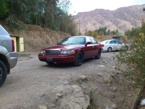 1998 Ford Crown Victoria - A maroon 1998 Ford Crown Victoria is parked on a dirt road with mountains in the background.