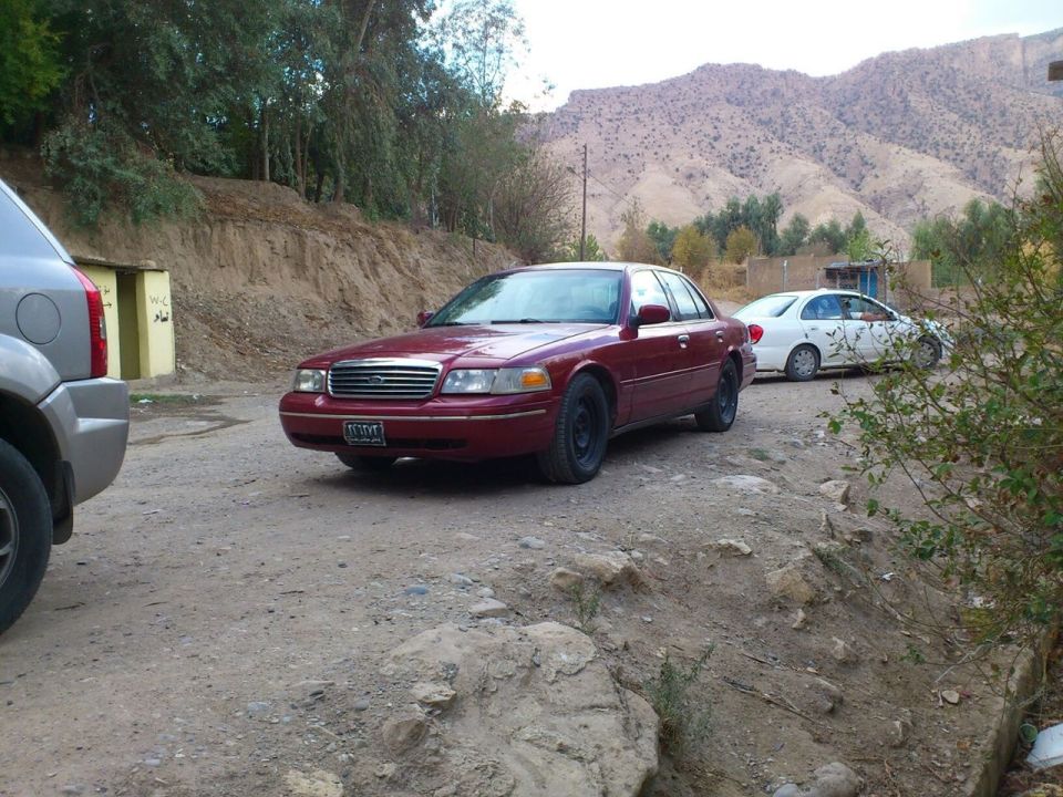 Maroon 1998 Ford Crown Victoria parked on a dirt road, front 3/4 view. Black wheels, some dirt on body