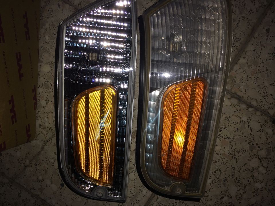 Two vehicle headlights, one with a TYC box behind it. The other headlight has a Supermotors watermark