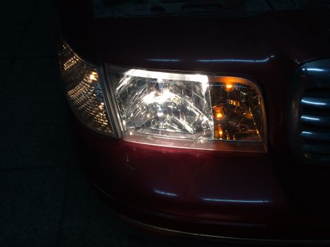 1998 Ford Crown Victoria - The front headlight assembly of a red 1998 Ford Crown Victoria, with the turn signal lit.