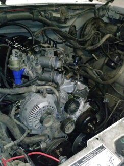 1995 Ford Bronco - Close-up view of a V8 engine, showing the alternator, carburetor, and various hoses and wiring.