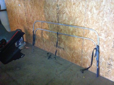 1982 Ford Bronco - A chrome roll bar with black straps is stored indoors against a wood-paneled wall.