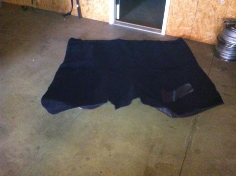 1982 Ford Bronco - Black carpet is spread out on the floor of a garage, with some stacked metal rims visible to the right.