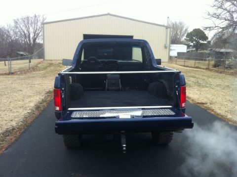 1982 Ford Bronco - Rear view of a blue SUV with its tailgate down, revealing a carpeted cargo area and a spare tire.