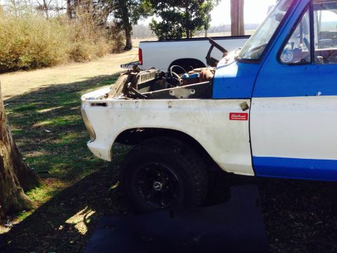 1979 Ford Bronco - A white and blue Ford truck, likely from the 1970s, sits in a grassy area with its hood open.