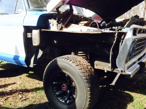 1979 Ford Bronco - The front fender and wheel of a 1979 Ford Bronco are visible, with the hood open and the vehicle in a state of disrepair.