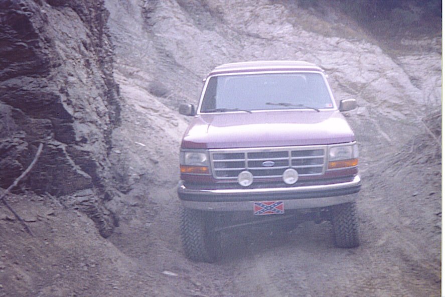 Purple 1992 Ford Bronco driving on a dirt road with rocky hillsides