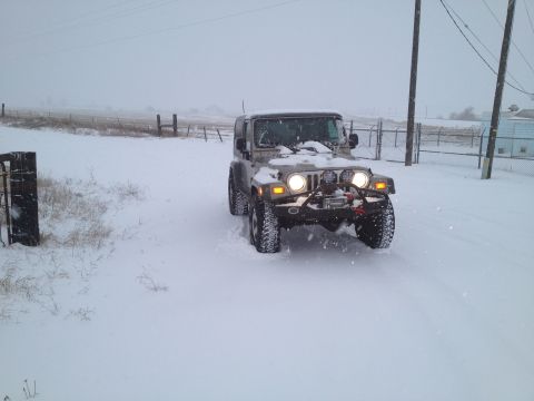 2005 Jeep Wrangler - A tan 2005 Jeep Wrangler navigates a snowy landscape with its headlights and auxiliary lights illuminated.