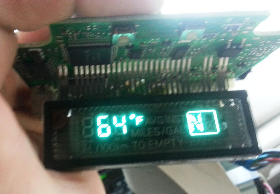 Ford overhead console display module in hand, VFD lit showing 64°F, circuit board exposed