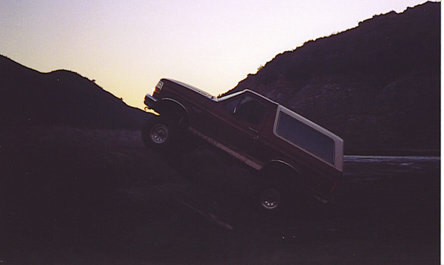Ford Bronco climbing a dirt hill at sunset