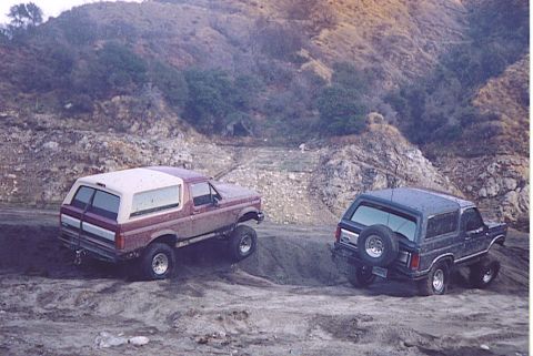 1992 Ford Bronco - Two Ford Broncos navigate a challenging off-road terrain with steep, rocky inclines.