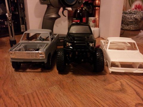 1995 Ford Bronco - Three model pickup trucks are displayed on a wooden floor, with one having its hood open.