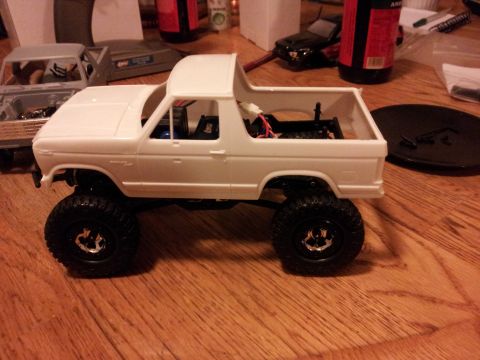 1995 Ford Bronco - A white remote-controlled Bronco model sits on a wooden surface, with parts and other models nearby.