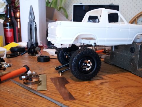 1995 Ford Bronco - Model car parts and tools are scattered across a workbench next to an unpainted vehicle chassis.