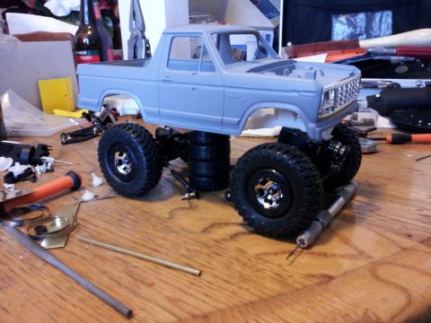 1995 Ford Bronco - A partially assembled model truck chassis with a Bronco body sits on a workbench, surrounded by tools and parts.