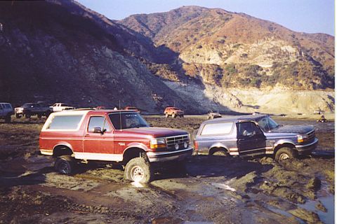 1992 Ford Bronco - Two Ford Broncos, a red and a blue one, are stuck in the mud at the bottom of a canyon.
