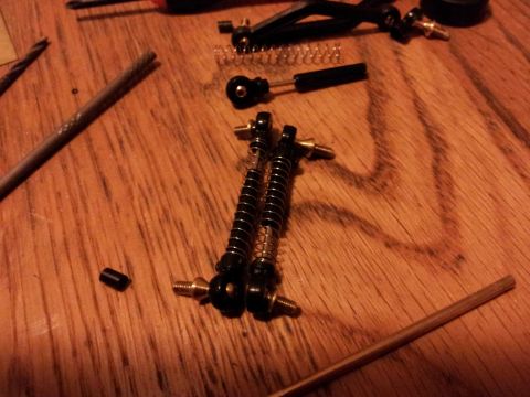 1995 Ford Bronco - RC car shock absorbers and springs laid out on a wooden table with other parts.