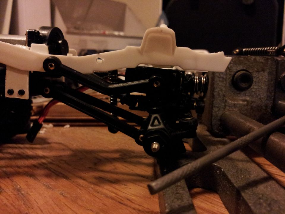 RC car chassis assembly with suspension parts attached, held in a vise