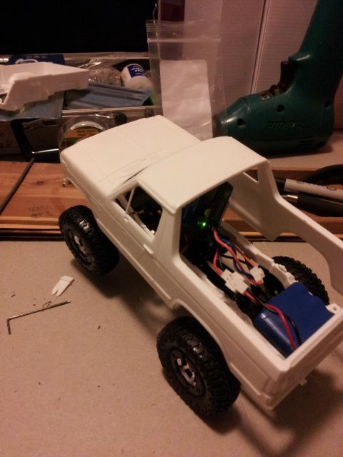1995 Ford Bronco - A white remote-controlled truck model is shown with its hood and bed open, revealing internal wiring and a battery.