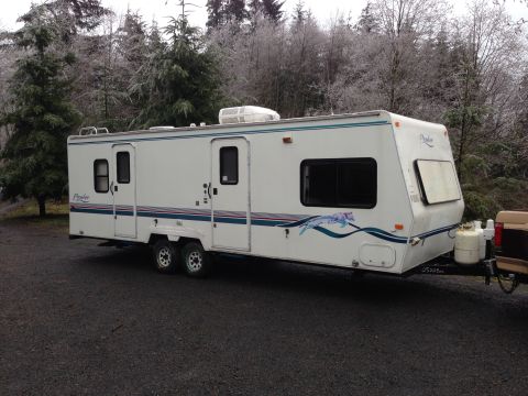 1988 Ford F-350 - A white travel trailer with blue and pink stripes is parked on a gravel surface with trees in the background.