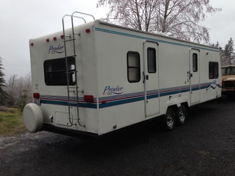 1988 Ford F-350 - A travel trailer is parked next to a pickup truck on a gravel surface under an overcast sky.