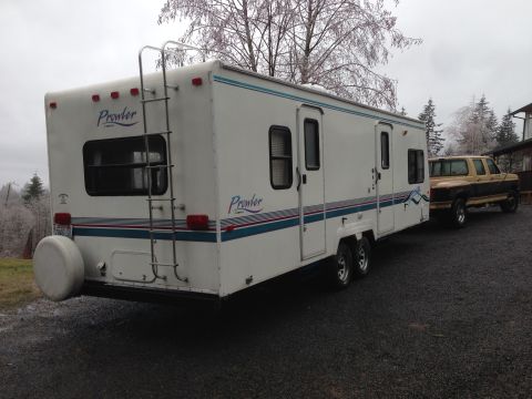 1988 Ford F-350 - A Prowler travel trailer is hitched to a two-tone pickup truck, parked on a gravel surface under an overcast sky.