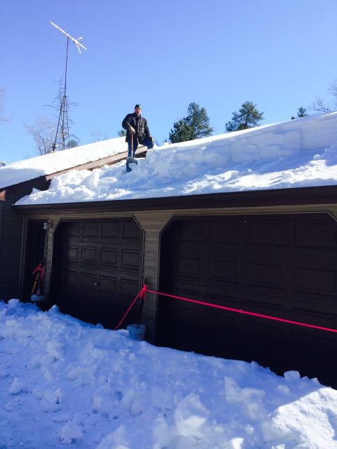 1978 Ford Bronco - A person clears heavy snow from a residential roof above two closed garage doors.