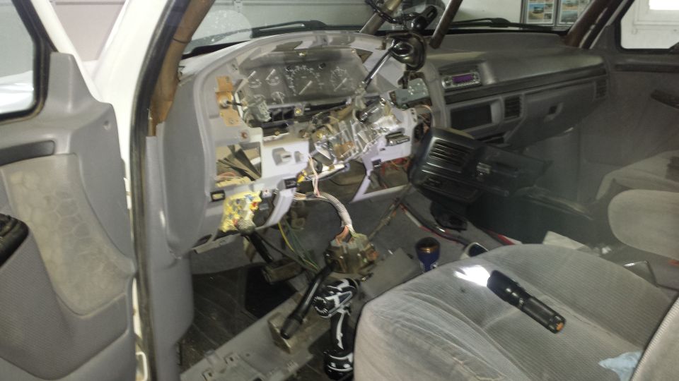 Vehicle interior with dashboard removed, showing wiring and components. A flashlight rests on the passenger seat