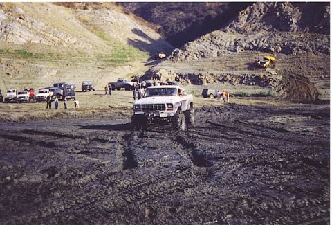 1992 Ford Bronco - Multiple vehicles are present at a muddy off-road event, with one truck prominently featured.