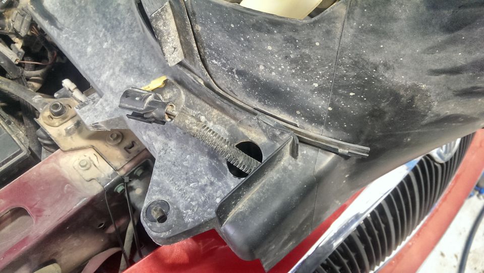 Black plastic engine bay component with a wire connector and a ribbed hose
