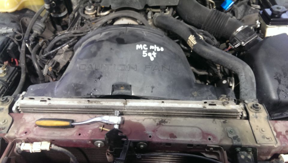 Engine bay showing fan shroud with handwritten 'MC 11/20 5qt' and 'CAUTION FAN' text