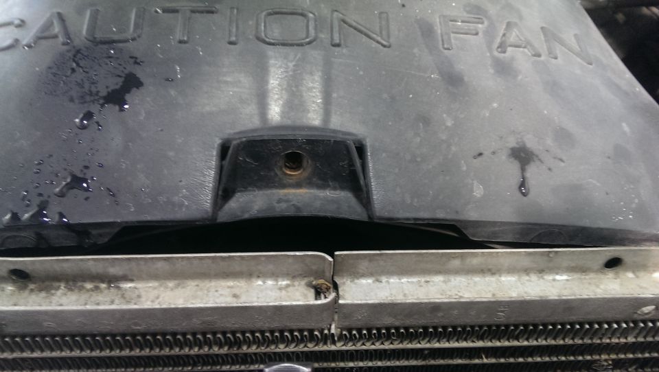 Close-up of a radiator fan shroud with 'CAUTION FAN' text. Some liquid is dripping