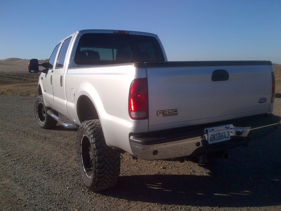 Silver Ford F-350 pickup truck, lifted with large tires, parked on a dirt road