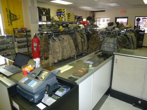 1992 Ford Mustang - A store interior displays racks of camouflage clothing and tactical gear, with a cash register and laptop on the counter.