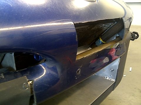 1995 Ford Probe - Close-up of a blue car's fender, showing a large, open vent with visible internal parts and some damage.